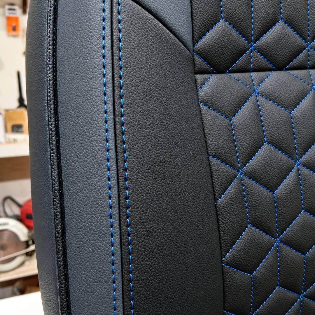 Gros plan d'un siège refait en simili cuir noir, surpiqûres bleues en losanges
